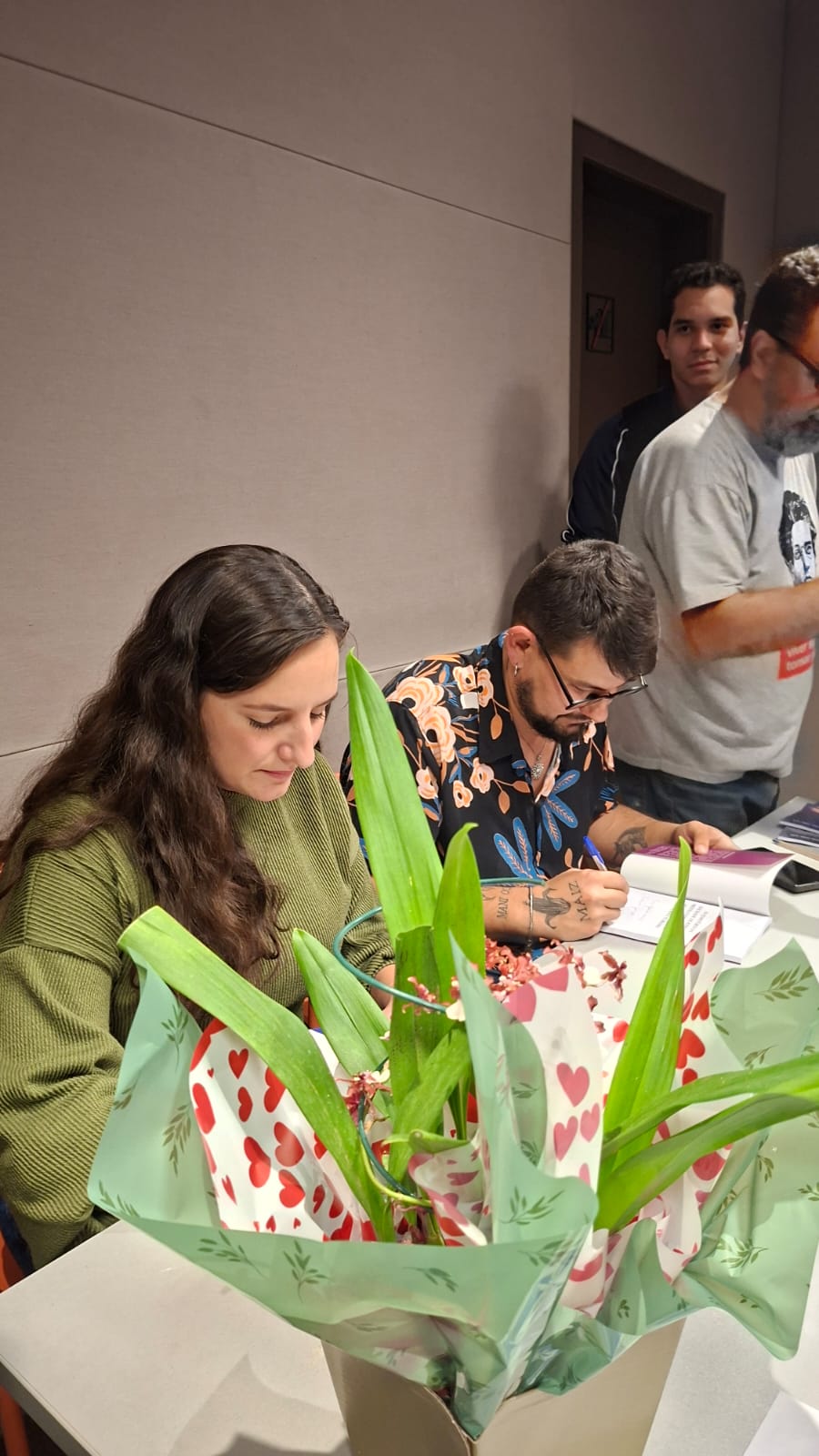Autora e autor autografando exemplares dos livros